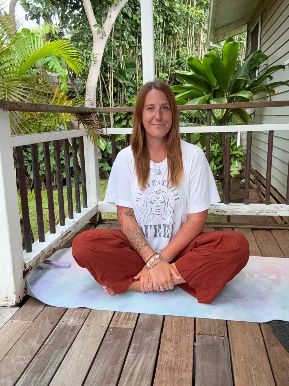Katrin sitzt lächelnd im Schneidersitz auf ihrer Yogamatte auf einer Veranda auf Hawaii, dahinter Palmen